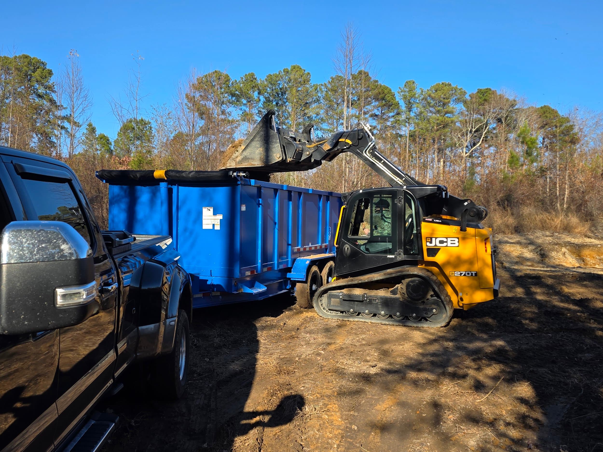 Track loader clearing a site to a roll-off